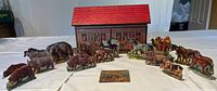 Photo showing the cardboard and wood Noah's Ark model with red roof and multiple pairs of animal figurines arranged in front.