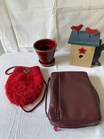 Full group photo showing all 4 items on a white cloth background: Bible in burgundy cover, ceramic cache pot, painted wooden birdhouse, and red felted purse.