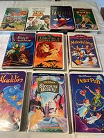 Top view of 10 Walt Disney VHS tapes arranged in two rows showing colorful covers including Saludos Amigos, Toy Story 2, Fantasia, Bambi, The Black Cauldron, The Lion King II: Simba's Pride, Melody Time, Aladdin, Sleeping Beauty, and Peter Pan.