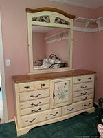 Front view of the Country Reflection dresser showing the cream paint, natural wood top, hand-painted floral center door, and black handles, with mirror on top.
