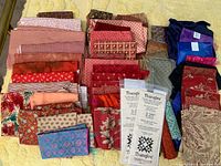 Overview of fabric lot showing multiple folded fabrics predominantly in red tones with two clear Thangles packages visible in center