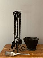 Photo of cast iron fireplace tool holder with four utensils and aluminum shovel in front, coal bucket to the side.