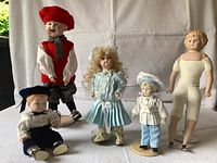 All five porcelain dolls with varied outfits and two standing dolls visible in front
