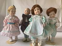 Four porcelain dolls standing on their individual stands, showing full outfits and poses.