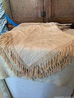 Square linen table topper with embroidered/printed pattern and thick cream lace fringe with tassels.