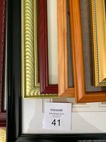 Overhead photo of eight assorted picture frames in various finishes and colors showing carved wood, metallic gold, burgundy, black, and natural wood tones.