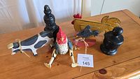 Top-view photo of 3 wooden farm animals and 2 black wooden finials on wooden table.