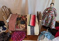 Wooden bed with patchwork quilt and multiple blankets; Hope Doll standing beside bed dressed in floral dress