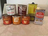 Front view of all cans showing labels with wood stains, varnish, fuel, and metal polish.
