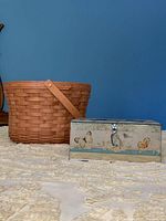 Photo showing the large round Longaberger basket next to the butterfly metal box on a patterned light rug with blue wall background