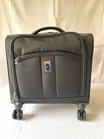 Front view of small black suitcase with logo plaque and spinner wheels.