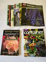 Lot of 16 Master Gardener journals and 2 gardening books laid out on white surface, showing colorful plant-themed covers.