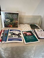 Photo showing a group of gardening books and resources spread on a table, including the Sustainable Gardening handbook, plant identification guides, landscape problems, and insect booklets.