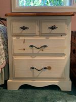 Front view of nightstand showing cream body, maple top, and four drawers with brass handles.