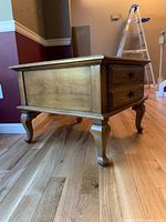 Photo of side view of one solid wood end table showing carved cabriole legs and panel detail on sides.