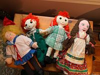Four handmade rag dolls arranged on wooden surface showing different clothing styles and hair colors.