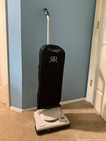 Full view of the Riccar SupraLite upright vacuum cleaner with black fabric bag and metal handle.