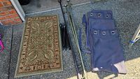 Photo showing green decorative rug, three curtain rods (two dark rods and one bronze collapsible rod), and two dark-colored curtain panels with grommets.