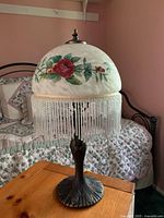 Full view of the lamp showing dome-shaped shade with hand painted roses and beaded fringe, sitting on wooden table.