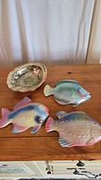 Top view of three ceramic fish and one ceramic shell dish on a wooden surface, showing their shape, colors, and textures, confirming pastel iridescent glazes and size estimation.