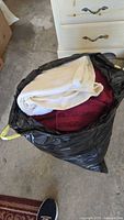 Black bag filled with assorted used towels in white and burgundy colors, showing towel texture and different sizes.