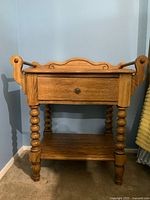 Front view of traditional oak wooden side table showing the drawer and lower shelf with spindle-turned legs.