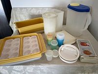 Wide shot of entire lot showing Tupperware loaf pans, deviled egg carrier, ice cream container, juice pitcher, small containers, Sterilite pitcher, hamburger press, egg poacher, and hotdog cooker box.