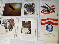 12 United States Mint souvenir stamp sets from the 1970s displayed on a white surface, showing cover envelopes with images of a bald eagle, American historical figures, Apollo 15 spacecraft, and George Mason.