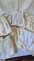 Grouped assortment of vintage baby and doll clothes in white and cream on table