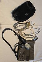 Photo of two stethoscopes with a blood pressure cuff and black carrying case laid out on a flat surface.