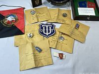 Overview of pennant, patch, six badges on envelopes and part of plate