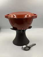 fondue pot with lid on stand and ladle in foreground