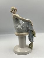 Front angled view of porcelain figurine seated on pedestal