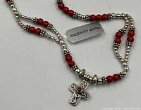 Close-up of necklace showing red beads, silver spacer beads, cross pendant, and 925 tag