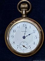 Front view showing entire watch face with Arabic numerals, blue hands and gold case