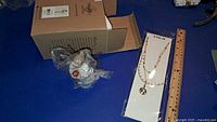 Angel figurine, necklace in package, box, ruler for scale