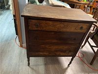 Front view of wooden dresser showing three drawers and turned legs