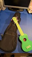 Green soprano ukulele on blue surface with black Stagg gig bag