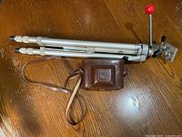 Folded aluminum tripod with red handle and leather camera case