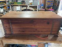 Front view of cedar chest on workbench showing metal straps, keyhole, full length lid