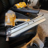 Photo showing two Bostitch N80 pneumatic framing nailers in yellow with metal magazines, placed on a black surface showing wear and dirt from use.