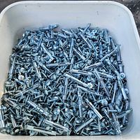 Top view of the full pail showing a dense quantity of shiny metal fasteners, including screws and toggle anchors, packed together.