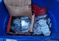 Box and blue container holding assorted steel plates, brackets, and multiple red circular saw blades.