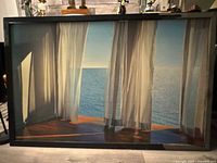 Framed print of ocean view through sheer curtains with polished wood floor shadows.