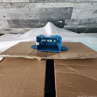 Close-up of a single blue KORA SPB2001R electrical box showing mounting brackets and holes.