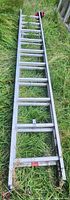 Full length view of the aluminum ladder laid flat on grass showing rungs and bottom support structure.