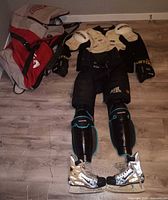 Full set of men's ice hockey gear laid out including Sherwood shoulder pads, padded black hockey pants, Game868 shin guards, Easton gloves, Nike Zoom skates with TUUK blades, and Bauer hockey bag.