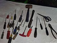 Mixed hand tools spread out on a surface including screwdrivers, hammers, scissors, pliers, and a stapler.