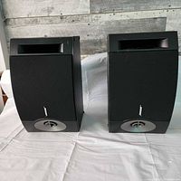 Two black Bose 201 V bookshelf speakers side by side on a white cloth surface, with a visible curved front panel and port opening at top, capturing the speakers' front view.