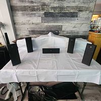 Front view of five satellite speakers and one center channel speaker arranged on a table with white cloth.